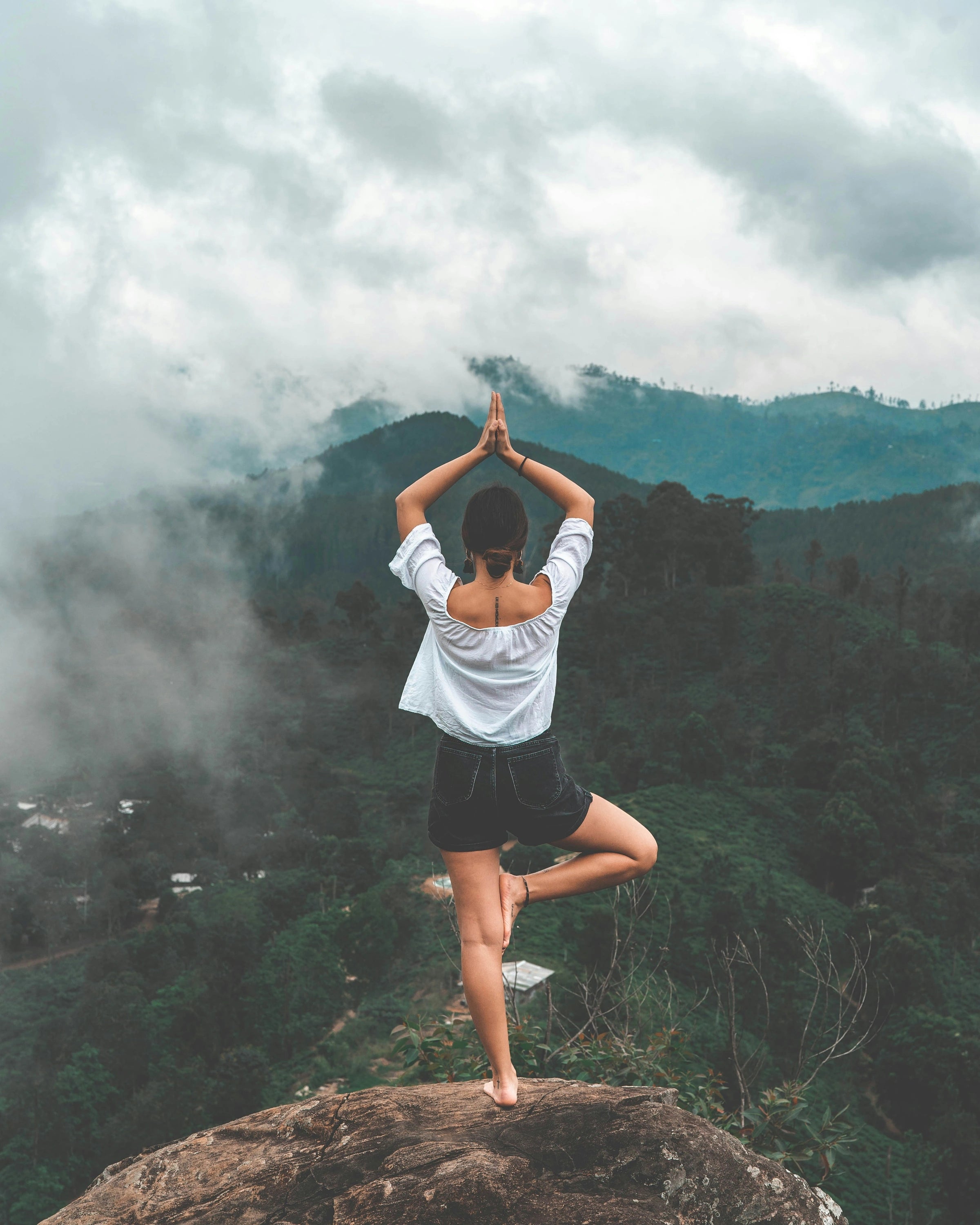 Woman practising yoga above misty forested mountains