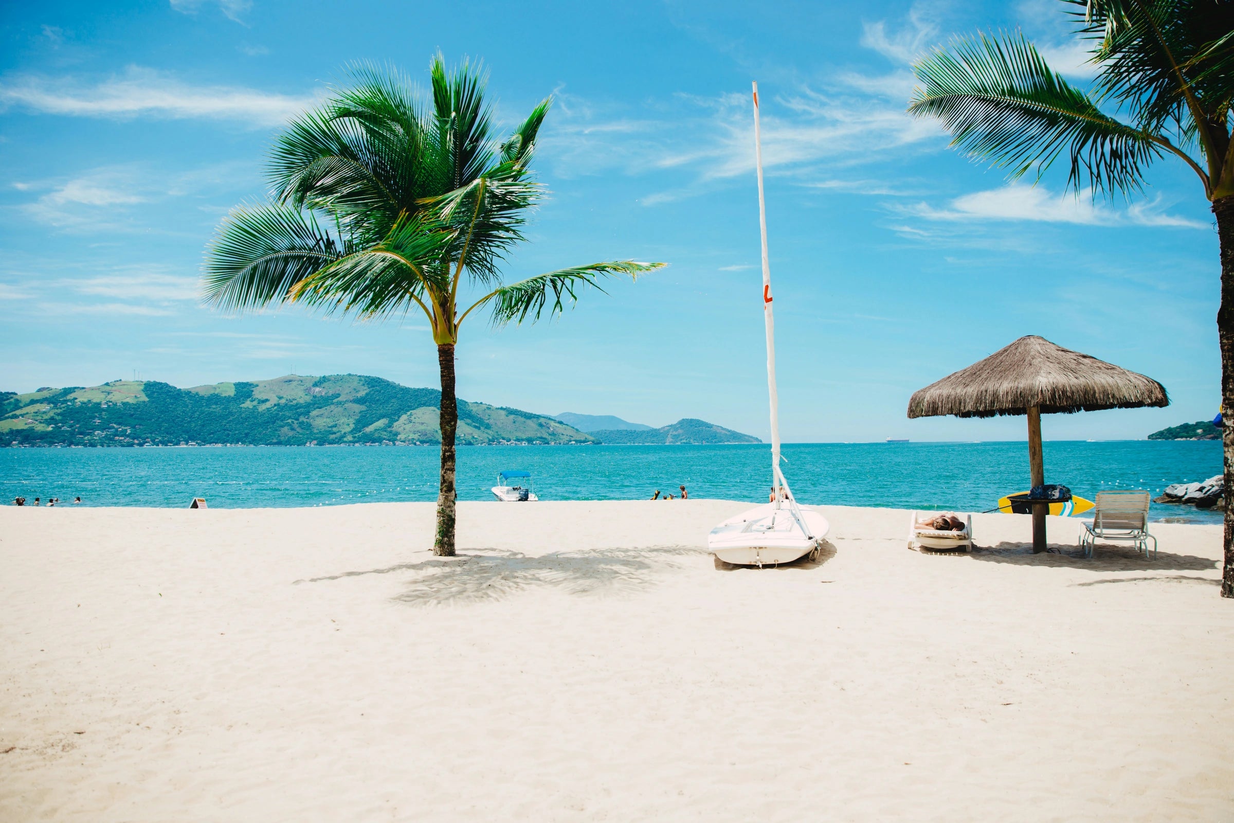Palm-lined tropical beach with a sailboat